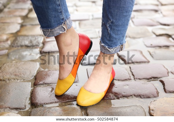 Woman in stylish blue ripped jeans\
walking down the rainy wet city street in colored ballet flats.\
Street fashion look. Legs of a young girl on the wet\
pavement
