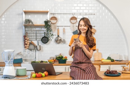 Woman in a stylish kitchen use smartphone with fresh healthy foods cooking health and wellness, fresh produce like grapes, apples, nutrition, sharing social media, look new recipe, healthy choices - Powered by Shutterstock