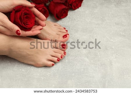 Woman with stylish red toenails after pedicure procedure and rose flowers on grey textured floor, top view. Space for text