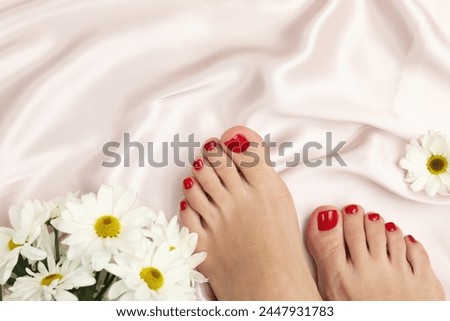 Woman with stylish red toenails after pedicure procedure and chamomile flowers on light silk fabric, top view. Space for text