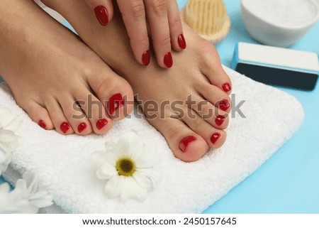 Woman with stylish red toenails after pedicure procedure and chamomile flowers on light blue background, closeup