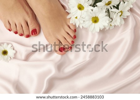 Woman with stylish red toenails after pedicure procedure and chamomile flowers on light silk fabric, top view. Space for text