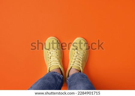 Woman in stylish sneakers on orange background, top view