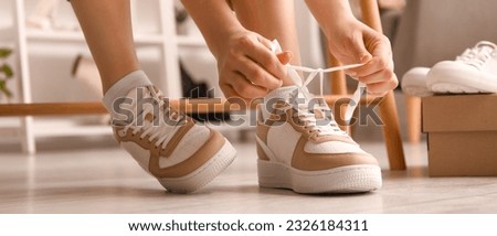 Woman in stylish sneakers tying shoe laces in shop
