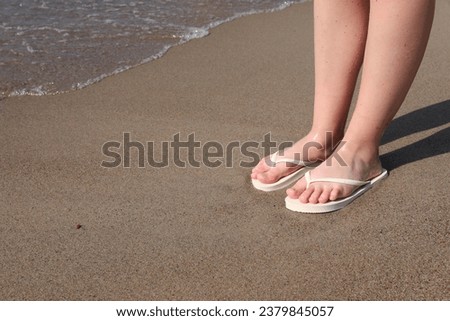 Woman in stylish white flip flops on sandy beach near sea, closeup. Space for text