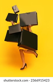 Woman in stylishly outfit carrying a lot of purchases, black shopping paper bags over yellow studio background. concept of fashion, beauty, salesperson, Black Friday, sale. copy space. ad