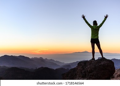 Woman successful hiking or climbing in mountains, motivation and inspiration in beautiful sunset landscape. Female hiker with arms up outstretched on mountain top looking at view.