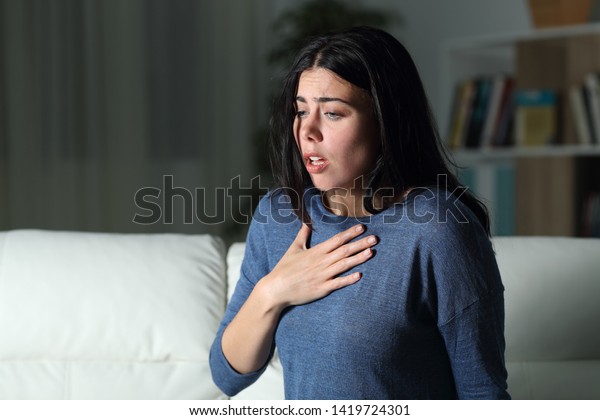 Woman suffering an anxiety attack alone in the night\
on a couch at home