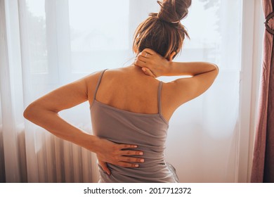 Woman Suffering From Back Pain While Sitting On Bed.