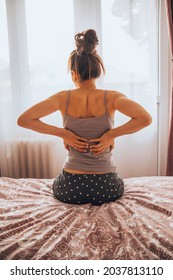 Woman suffering from back pain while sitting on bed.	 - Shutterstock ID 2037813110
