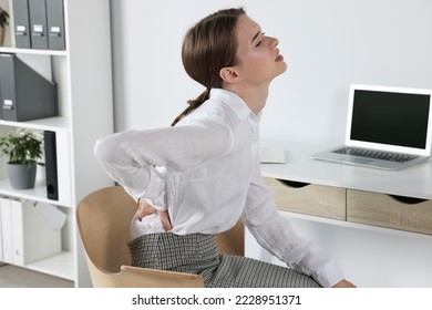 Woman suffering from back pain while sitting in office. Symptom of scoliosis - Shutterstock ID 2228951371