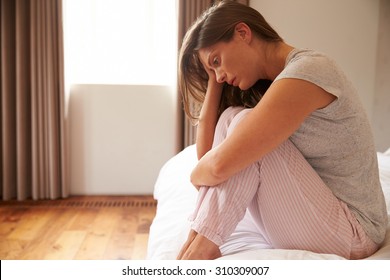 Woman Suffering From Depression Sitting On Bed In Pajamas - Shutterstock ID 310309007