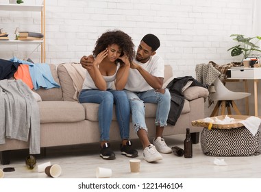 Woman Suffering From Hangover, Boyfriend Supporting Her, Sitting Together In Messy Room After Party