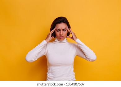 Woman suffering from headache, feeling strees. Studio shot, casual clothes, yellow background.
