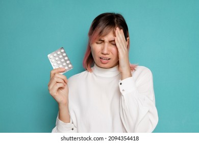 a woman suffering from a headache holds painkillers while standing on a blue background - Shutterstock ID 2094354418