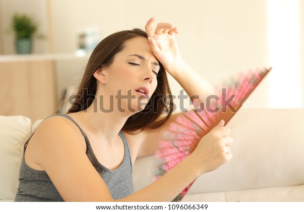 Woman suffering a heat wave using a fan
sitting on a couch in the living room at
home