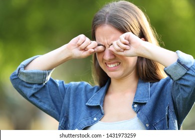 Woman suffering itching scratching eyes outdoors in a park