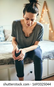 Woman Suffering From Knee Pain While Sitting On Bed. Focus On Face.