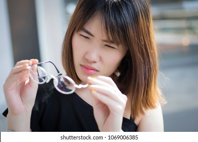 Woman Suffering From Poor Eye Vision; Portrait Of Asian Woman With Eye Problem Or Bad Blur Eye Sight Holding Eyeglasses, Concept Of Seeing Or Visual Disorder; Young Adult Asian Woman Model