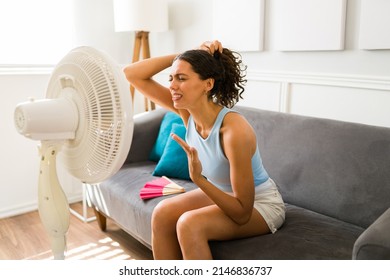 Woman Suffering Without An Air Conditioning. Upset Sad Woman Sweating And Suffering From A Heat Stroke While Using An Electric Fan