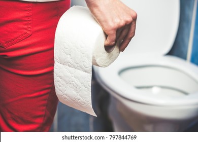 Woman suffers from diarrhea holds toilet paper roll in front of toilet bowl. Stomach upset.