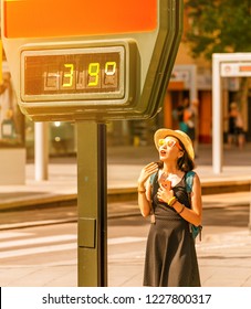 Woman Suffers From Heat And Sunstroke Outside In Hot Weather On The Background Of A Street Thermometer Showing 39 Degrees Celsius