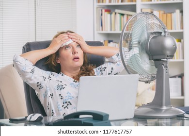 Frau leidet während der Arbeit im Büro an Hitze und versucht sich durch den Ventilator abzukühlen