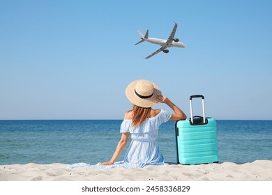 Woman with suitcase on beach looking at airplane flying in sky, back view - Powered by Shutterstock