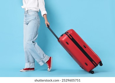 Woman with suitcase on light blue background, closeup