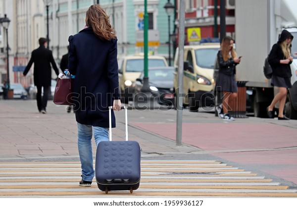 Woman with a suitcase on\
wheels walking on pedestrian crossing in city. Concept of travel,\
street safety