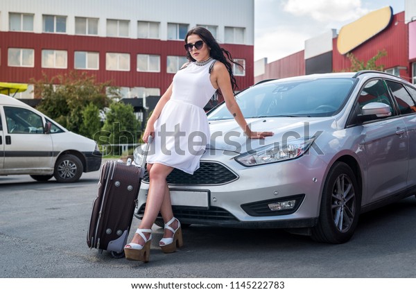 Woman with suitcase\
sitting on car bonnet