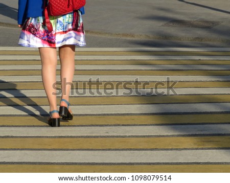 Woman in a summer dress crossing the street at a crosswalk. Female feet on a pedestrian crossing, street safety