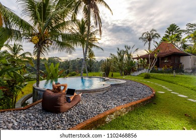 Woman summer freelance nomand work relaxing with laptop near swimming pool colorful beautiful outdoors. Traveling Bali with a computer wi-fi poolside nature tropical palms, always in touch concept - Powered by Shutterstock