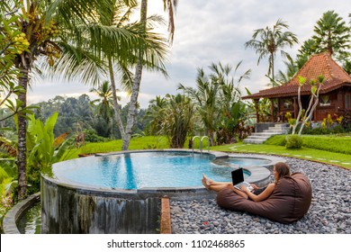 Woman summer freelance nomand work relaxing with laptop near swimming pool colorful beautiful outdoors. Traveling Bali with a computer wi-fi poolside nature tropical palms, always in touch concept - Powered by Shutterstock