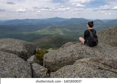 Woman at the summit of Wright Peak (High Peaks Wilderness Area, Adirondack Mountains). Looking out towards Heart Lake, surrounded by green forests, mountains in the distance (New York State, USA).