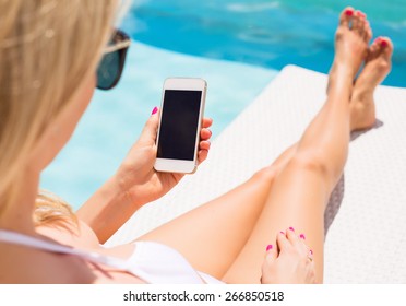 Woman sunbathing in chair by the pool and using mobile phone