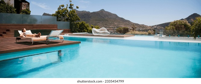 Woman sunbathing on lounge chair next to luxury swimming pool mountain view - Powered by Shutterstock