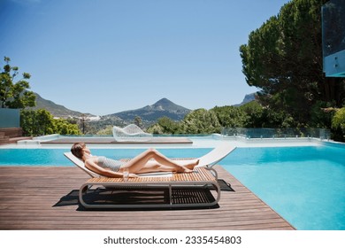 Woman sunbathing on lounge chair next to luxury swimming pool mountain view - Powered by Shutterstock