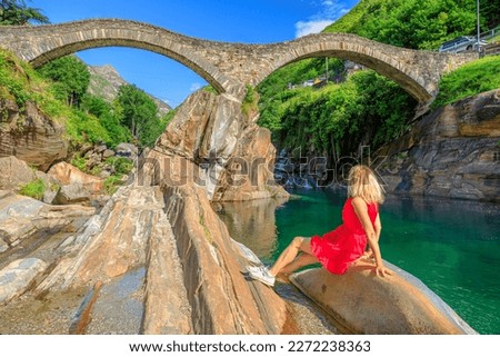 Woman sunbathing under Roman stone bridge: Ponte dei Salti over Verzasca River. Verzasca valley by Lavertezzo. Famous landmark for riverside leisure and high diving in Ticino, Switzerland.