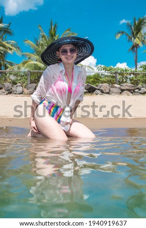 A woman in sunglasses, a colorful swimsuit and beach hat enjoys her time off at a tropical resort.
