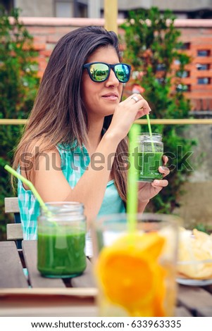 Frau mit Sonnenbrille, die im Freien grünen Gemüse-Smoothie trinkt.