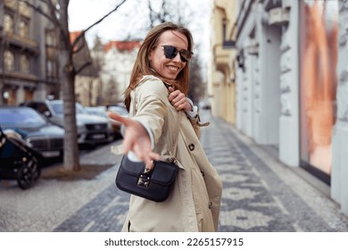 Woman in sunglasses extends his hand follow me on city street background . High quality photo