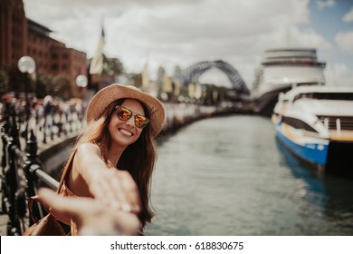 Woman in sunglasses holding boyfriend hand, while taking a photo of her, in Sydney Harbour. - Powered by Shutterstock