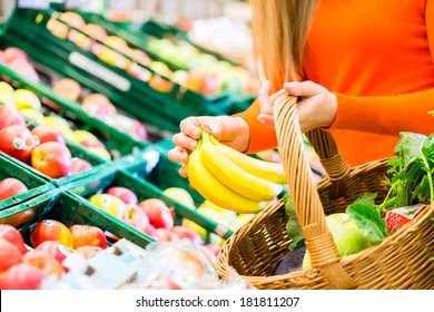 Woman in supermarket at the fruit shelf shopping for groceries, she is putting a banana in her basket - Powered by Shutterstock