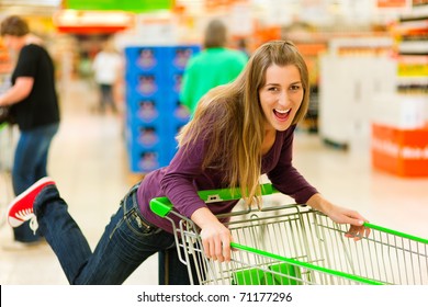 Woman In A Supermarket Running Trough The Aisle With A Shopping Cart And Having Fun