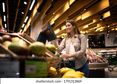 Woman At Supermarket Using Self Service Digital Scale To Measure The Weight Of Fruit. Food Buying At Grocery Store.