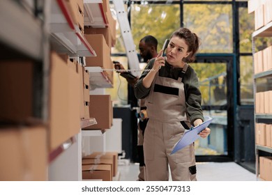 Woman supervisor talking at landline phone with remote manager, discussing products inventory in storehouse. Employee working at clients orders, preparing cardboard boxes for shipment - Powered by Shutterstock