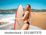 Woman surfer standing with surfboard at beach. Female surfer in bikini posing with surfboard near ocean. Surfgirl standing at water edge ready for surfing on sunny day.