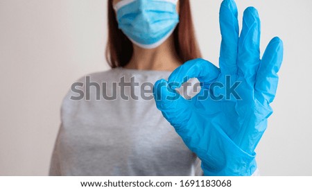Woman with a surgical mask shows by hands in latex glove a symbol OK.