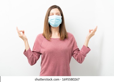 Woman with surgical mask trying to cope with stress and doing some meditation during covid19 pandemic - Shutterstock ID 1695580267